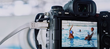 Usage image of the camera mounted on a tripod and connected to LAN cable, shooting water polo game with live view image displayed on LCD monitor