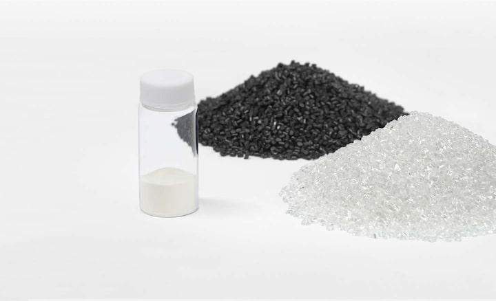 A small vial of white plastic granules next to a pile of black plastic granules and a pile of white ones