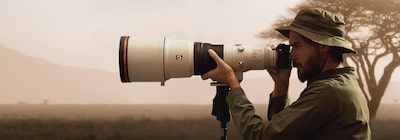 Image of a man looking through a tripod-mounted camera that is attached to a super-telephoto lens