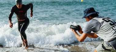 Usage image of a man holding the camera to shoot a triathlete running out of the sea